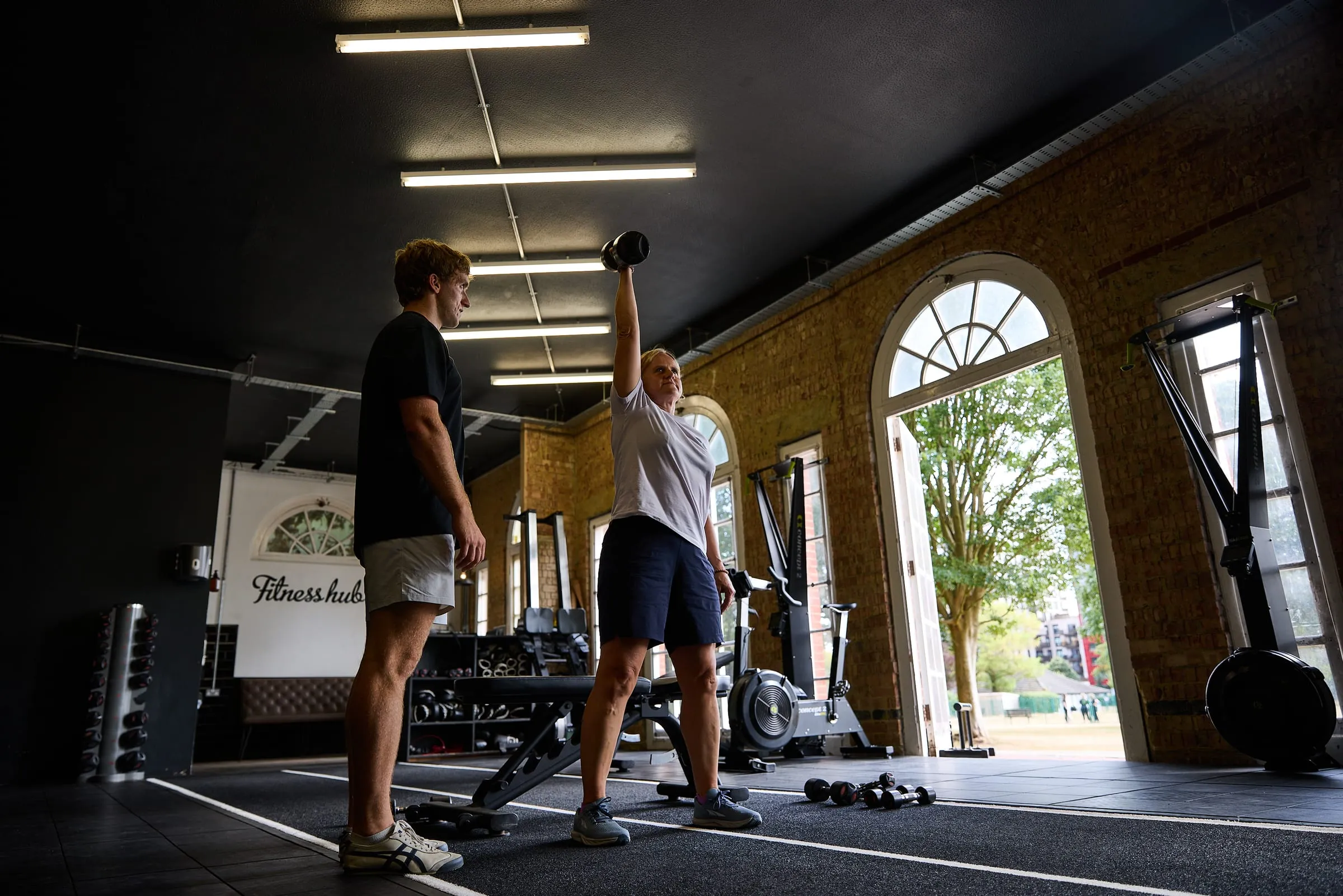 Felix coaching a client through a lift by the gym windows